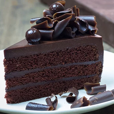 a dark chocolate layer cake with chocolate icing and chocolate curls, ona white plate