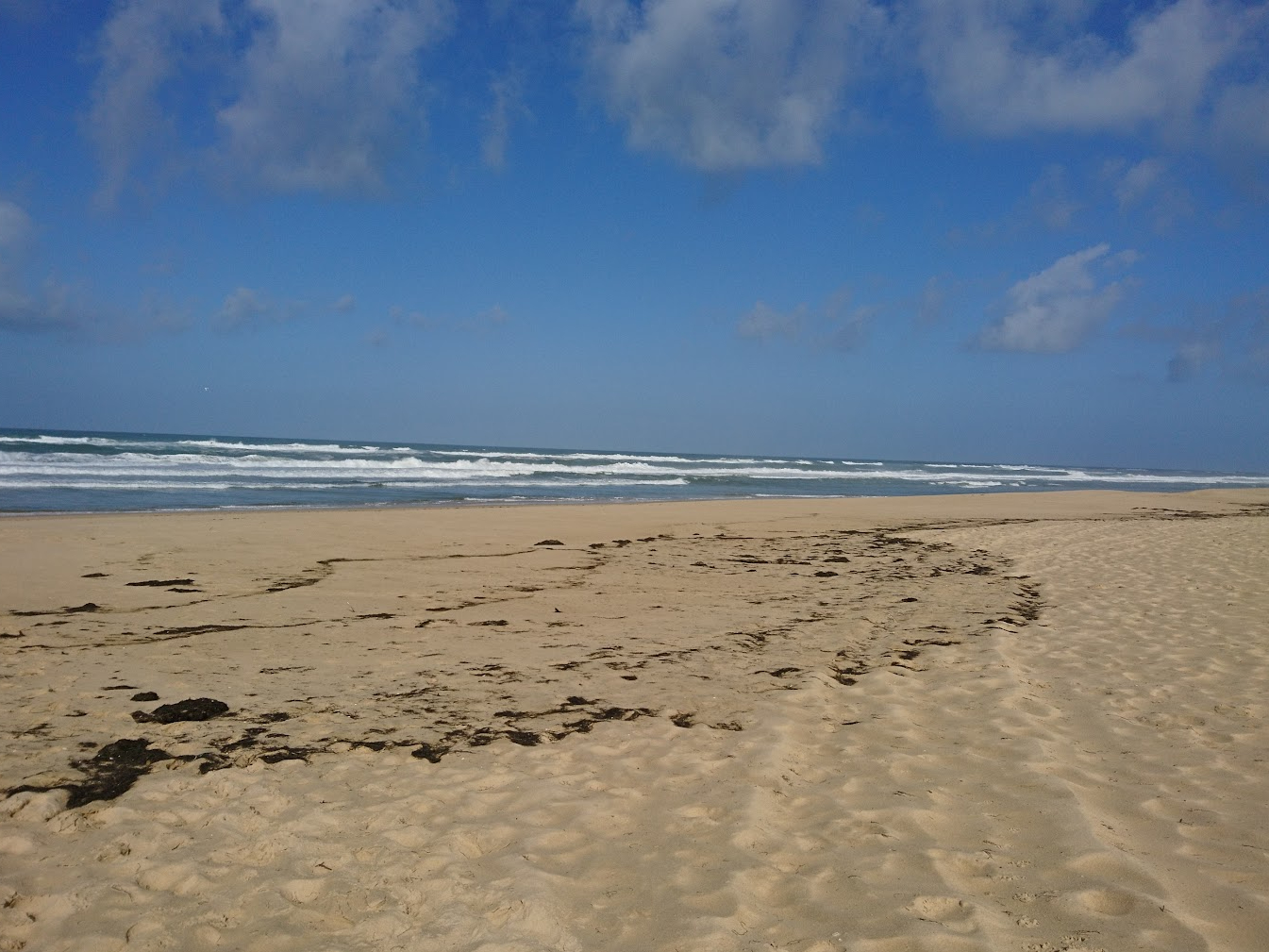 a wide sandy beach with some small waves in the sea, and no people around